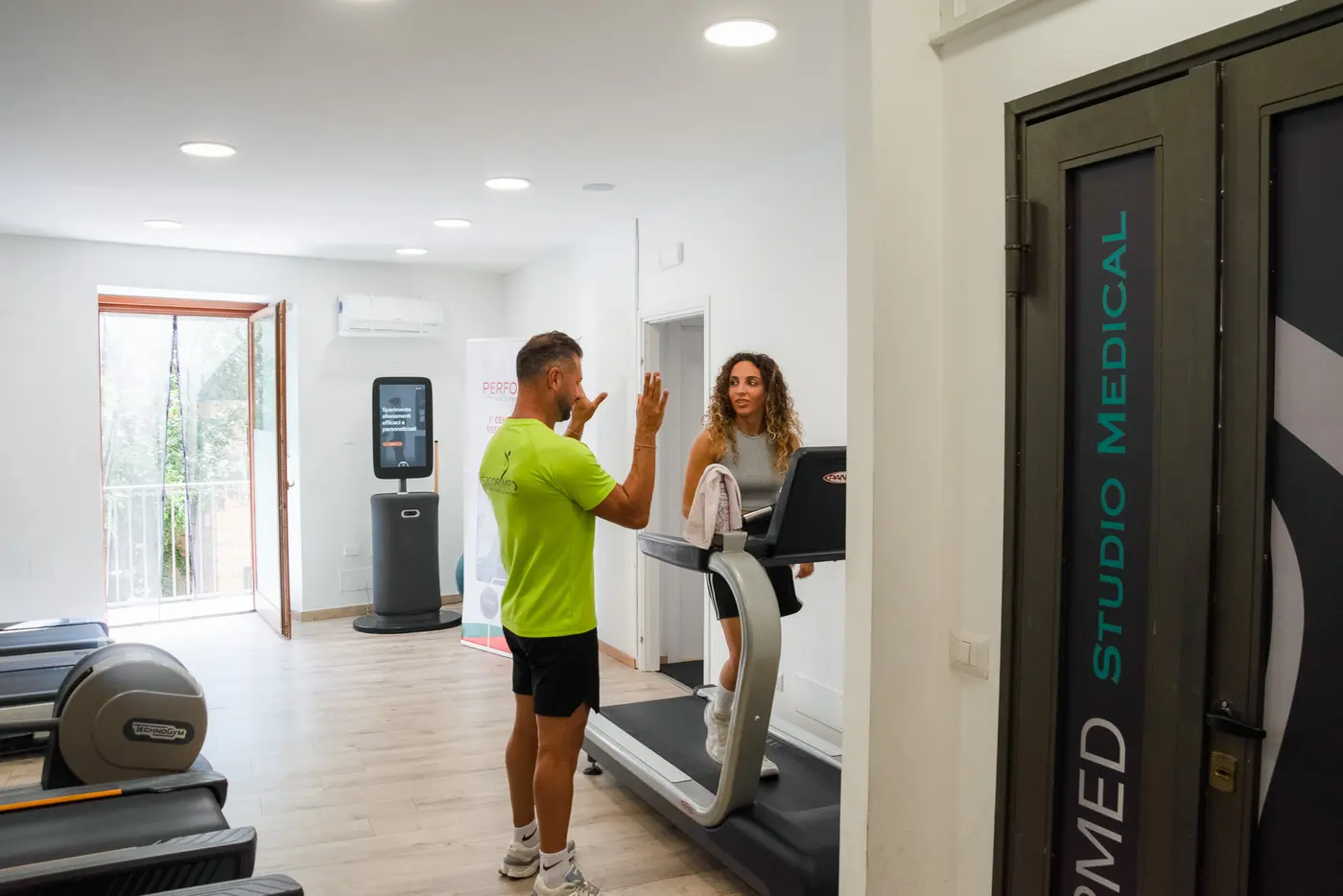 Un trainer parla con una cliente sul tapis roulant in una sala luminosa