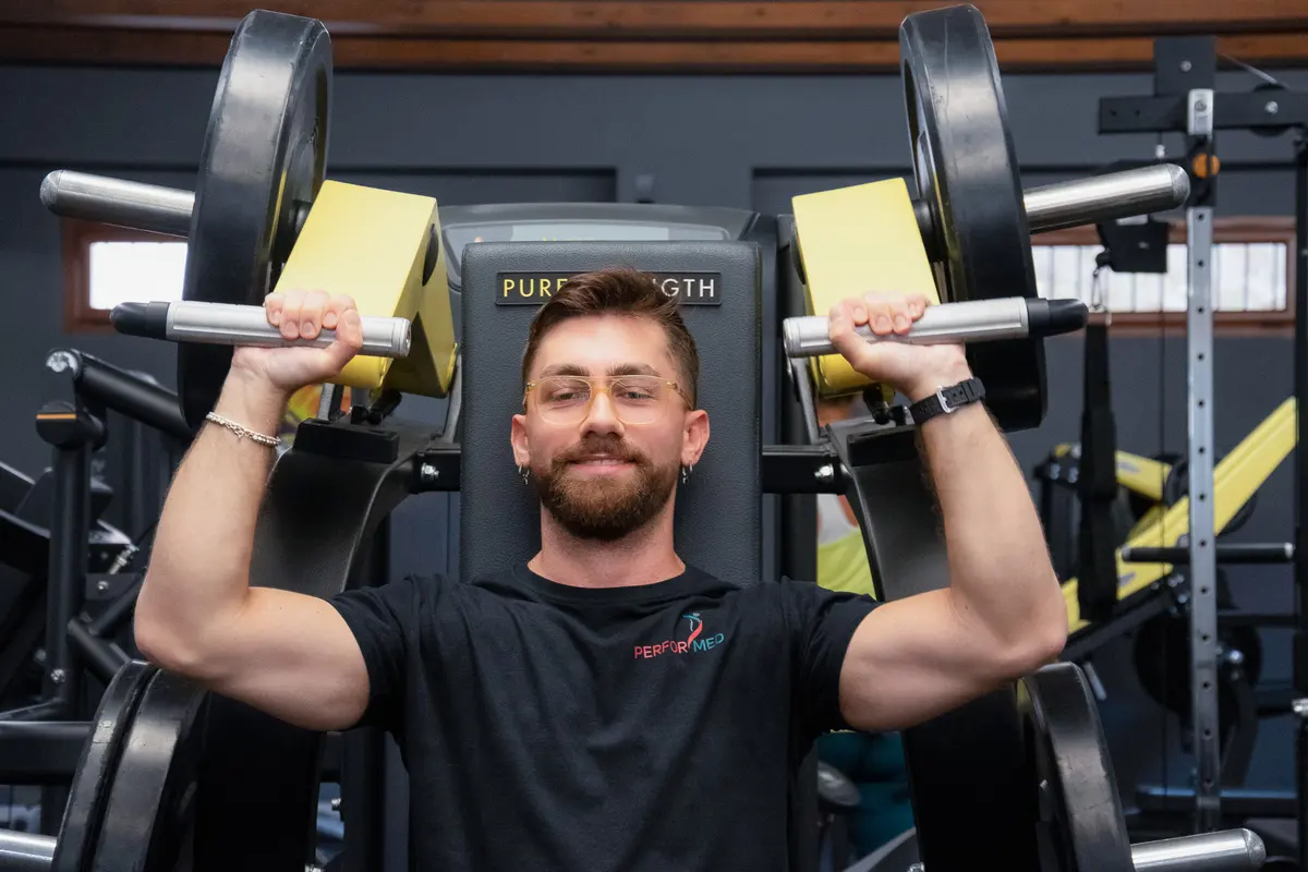 Un trainer sorride mentre usa la macchina per le spalle